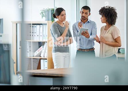 Exchanging ideas between meetings. Shot of office colleagues having a discussion over a digital tablet. Stock Photo