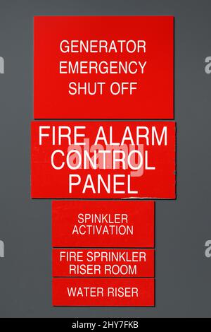 Collection of red and white fire emergency signs on gray wall featuring Generator emergency shut off, Fire alarm control, riser room Stock Photo