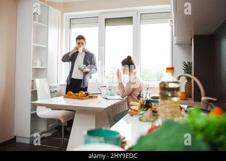 Successful caucasian couple drinking coffee and working on laptop together while sitting at home in the morning. Online lifestyle. Morning coffee. Stock Photo