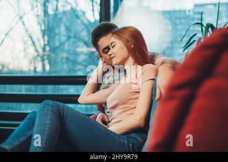 Woman and handsome man enjoying spending time together sitting on the sofa in living room. Stock Photo