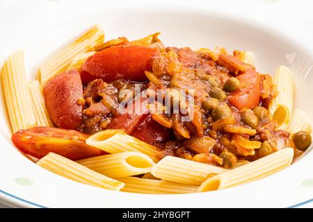 High angle view of penne pasta with tomato sauce with green pea, tomato and chicken in white ceramic dish. Stock Photo