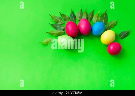 Pattern of colored eggs and green leaves on a green background. Copy space for text. Bright colours. Easter. Stock Photo