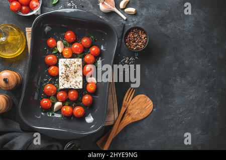 Fresh ingredients are prepared for baking fetapasta. Cherry tomatoes, feta cheese, garlic and herbs in a baking dish. Close-up. Stock Photo