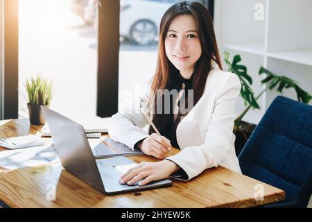A female entrepreneur or businesswoman showing a smiling face while operating a computer working on a wooden table. Stock Photo