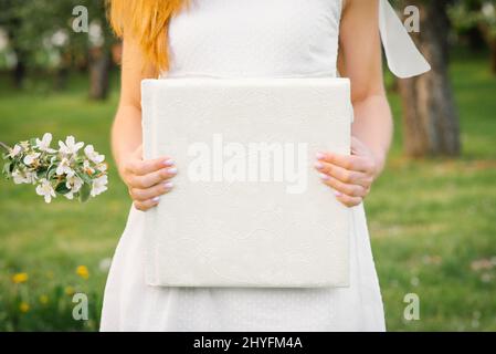 A white-covered wedding photo album is held by a woman in a white dress Stock Photo