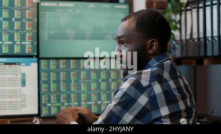 Male broker talking about forex trade sales statistics, working at multi monitors workstation with real time stocks. Market exchange numbers with investment fund share and capital profit. Stock Photo