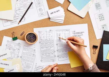 Web UX designer working at desk with several website wireframe sketches and sitemap. Website project concept. Flat lay Stock Photo
