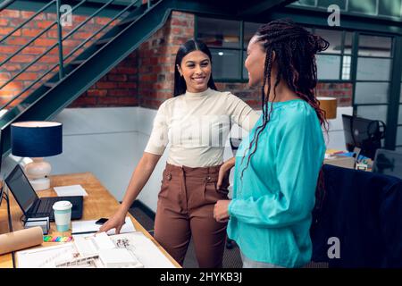 Happy multiracial young female architects discussing over blueprint while standing at desk in office Stock Photo