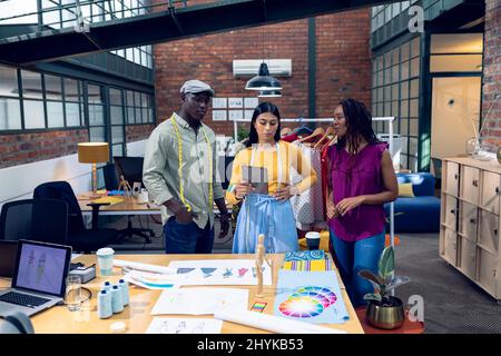 Multiracial young male and female fashion designers discussing design over digital tablet at desk Stock Photo