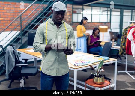 African american young male fashion designer using digital table while standing at workplace Stock Photo