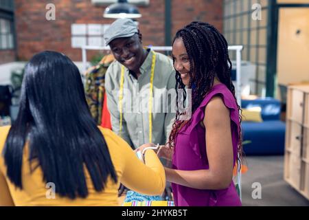 Smiling multiracial young male and female fashion designers talking while standing at desk Stock Photo