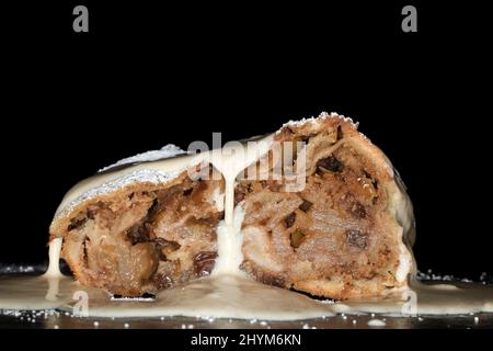 Apple strudel with sultanas, vanilla sauce and icing sugar, studio photography with black background Stock Photo