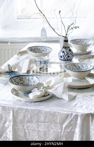 Elegant Easter table setting with empty painted porcelain tableware, plates and bowls, Easter eggs decorations, branches in vase on white tablecloth i Stock Photo