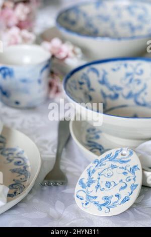 Elegant Easter table setting with empty marine ornament painted porcelain tableware, plates and bowls, Easter eggs decorations on white tablecloth. Ea Stock Photo