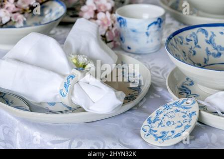 Elegant Easter table setting with empty marine ornament painted porcelain tableware, plates and bowls, Easter eggs decorations on white tablecloth. Ea Stock Photo