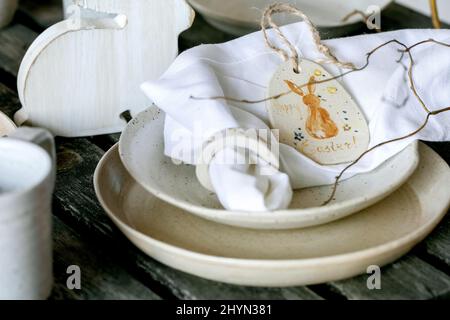 Rustic Easter table setting with empty craft ceramic tableware, plates and bowls, Easter bunny rabbit decorations, vase on wooden table. Easter holida Stock Photo