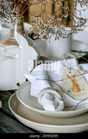 Rustic Easter table setting with empty craft ceramic tableware, plates and bowls, Easter bunny rabbit decorations, vase on wooden table. Easter holida Stock Photo