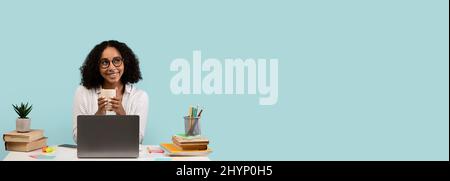 Smiling woman sitting at table with laptop, using cell phone Stock Photo