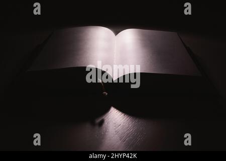 One open thick book on white table in the dark. Stock Photo