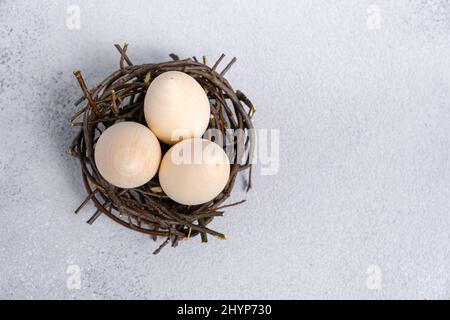 Three eggs in bird's nest made of branches on light gray textured background with copy space. Wooden eggs for creativity and coloring. Preparation for Stock Photo