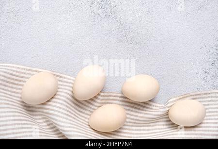 Five eggs on a striped linen napkin or towel on light gray textured background. Easter card in pastel colors with copy space. Wooden egg for Stock Photo