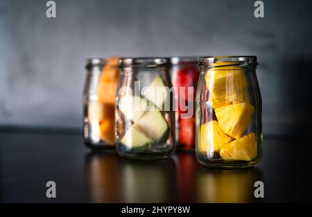 Variety small pieces of tropical fruits in cleared bottles on black table, each kind of fruit is separated into a glass bottle as snacks, blurred back Stock Photo