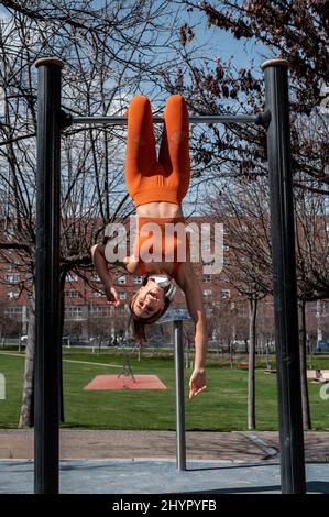 Attractive sporty woman with headphones around her neck doing stretching and balance exercises while Stock Photo