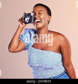 Modern time through a vintage lens. Studio shot of a beautiful young woman using a camera against a oink background. Stock Photo