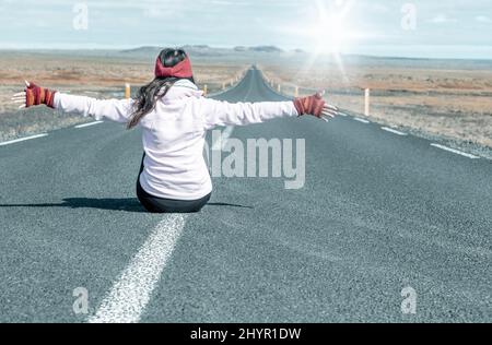 Traveller woman sitting on the road looking towards the sun. Strength and independence. Woman day. Tourism, freedom and holiday concept. Stock Photo
