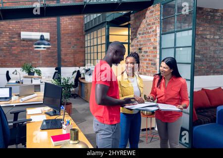 Smiling multiracial young business people discussing over documents while standing in office Stock Photo