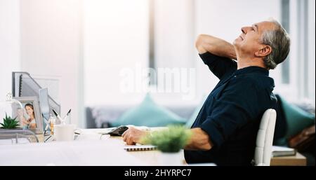 My neck is starting to give in now. Shot of a mature businessman suffering from neck pain while sitting at his desk at work. Stock Photo