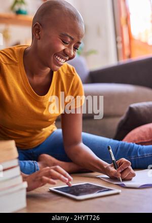 A young student sits on the floor studying with books and a tablet Stock Photo
