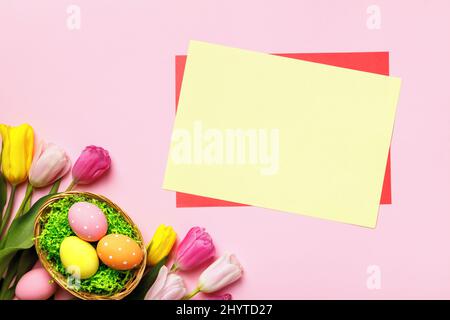 Easter card. Eggs in a basket flowers tulips empty sheet of paper with place for text on a pink background. Stock Photo