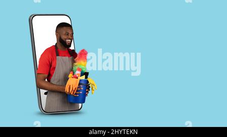 Black Male Cleaner With Basket With Detergents Peeking Out Of Smartphone Screen Stock Photo