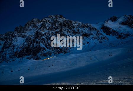 Silhouette of modern snowcat ratrack with led light preparing ski slope at night snow park with star sky at Shymbulak ski resort Almaty, Kazakhstan Stock Photo