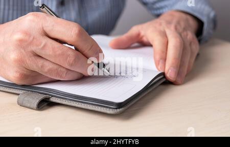 Man hands closeup taking notes in planner. Man sitting at table in office or at home, working or studying and writing agenda, thoughts, important information in organizer. High quality photo Stock Photo