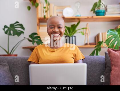 A young woman sits on the couch with her laptop and smiles Stock Photo