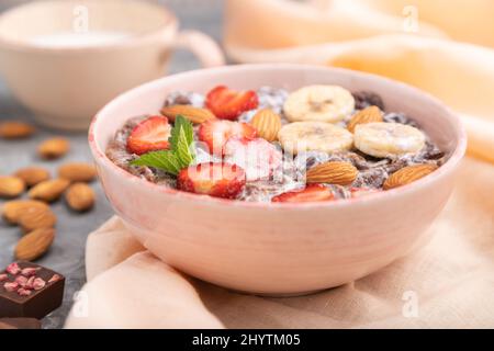 Chocolate cornflakes with milk, strawberry and almonds in ceramic bowl on gray concrete background and orange linen textile. Side view, close up, sele Stock Photo