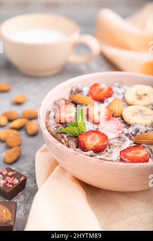 Chocolate cornflakes with milk, strawberry and almonds in ceramic bowl on gray concrete background and orange linen textile. Side view, close up, sele Stock Photo