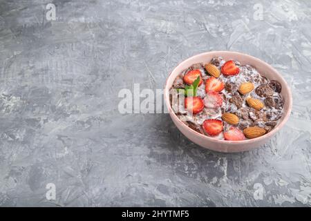 Chocolate cornflakes with milk, strawberry and almonds in ceramic bowl on gray concrete background. Side view, copy space. Stock Photo