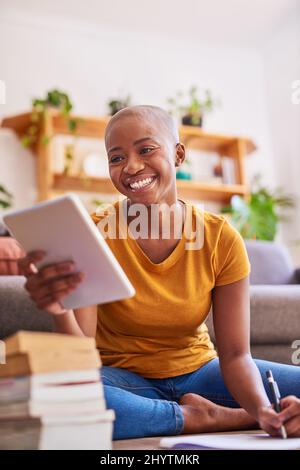 A young student sits on the floor studying taking notes from her tablet Stock Photo