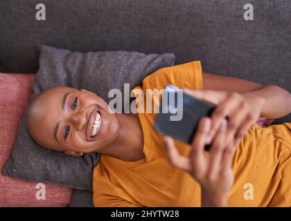 An overhead view of a young woman lying on the couch on her phone Stock Photo