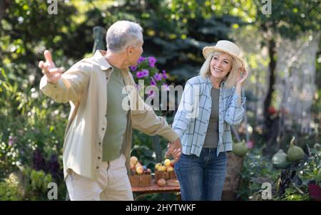 Happy loving senior couple holding hands and walking in their garden on warm spring day, enjoying time together Stock Photo