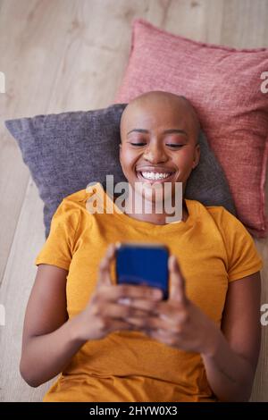 An overhead view of a young woman lying on the floor on her phone Stock Photo
