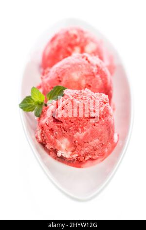 Three scoops of strawberry ice cream with mint leaves in a bowl Stock Photo