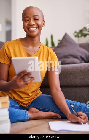 A young student sits on the floor studying taking notes from her tablet Stock Photo