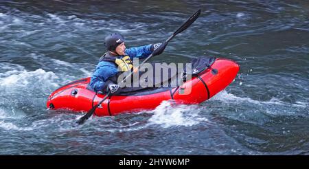 A man wearing a dry suit to protect him from the cold kayaking the Deschutes River in Oregon in a small kayak. Stock Photo