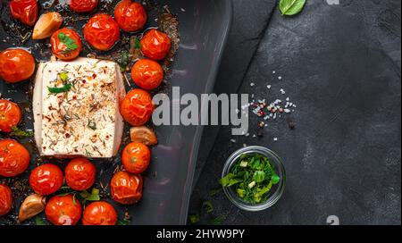 Baked feta cheese and cherry tomatoes on a black background. Close-up. Stock Photo