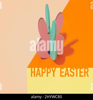 text happy easter and an easter bunny cut out on thin plywood painted in different colors, on an orange, yewllo and pale brown surface creating a visu Stock Photo