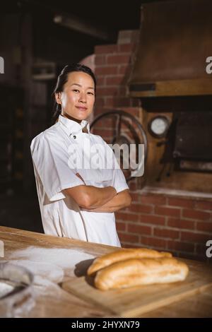 Portrait of confident mid adult asian female baker with arms crossed standing in bakery Stock Photo